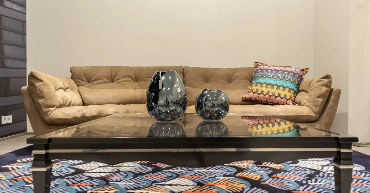 Un salon contemporain avec un canapé beige, des coussins colorés et des vases réfléchissants sur une table en verre.