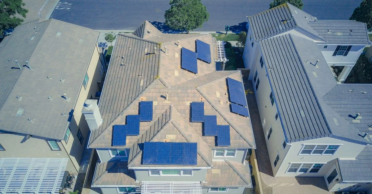 Vue aérienne de maisons suburbaines équipées de panneaux solaires dans un quartier ensoleillé.