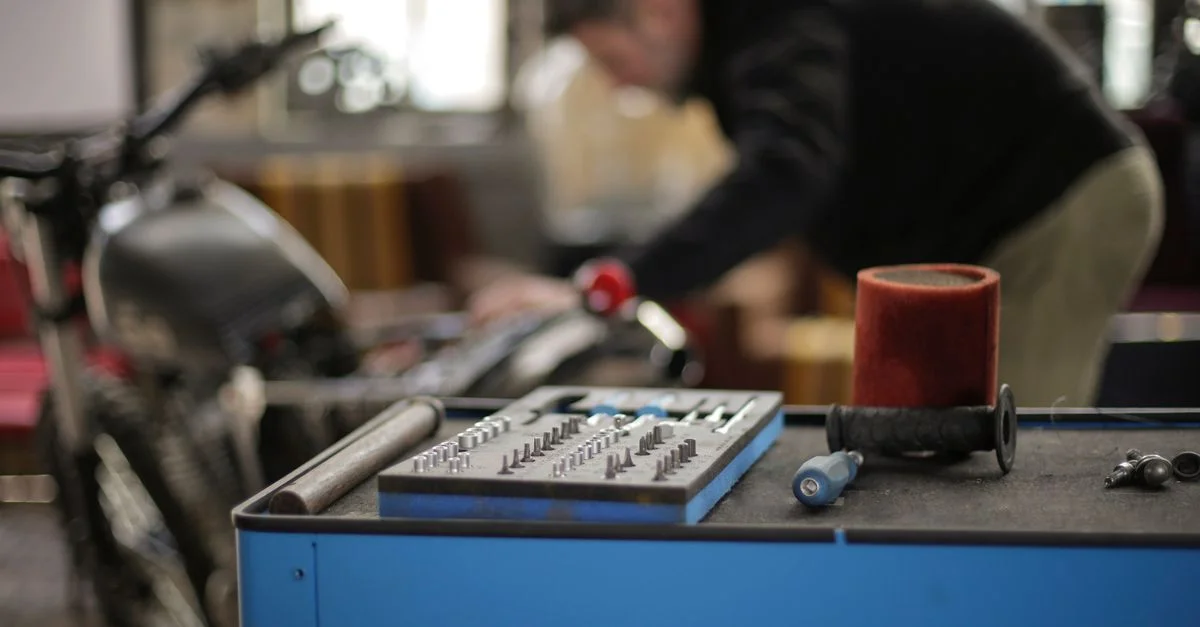 Un mécanicien travaille sur une moto dans un atelier, équipé de divers outils et équipements.